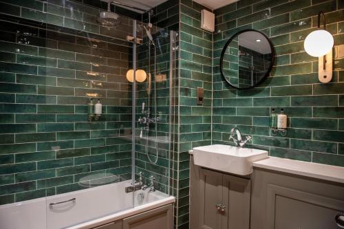 Baño de azulejos verdes con lavabo y espejo en The Red Lion Inn by Chef & Brewer Collection en Todwick