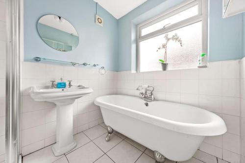 La salle de bains blanche est pourvue d'un lavabo, d'une baignoire et d'un miroir. dans l'établissement Spacious 3 bed house in North Leeds perfect for families & longer stays, à Adel