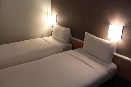 two beds in a room with two lamps on the wall at ibis Thornleigh in Thornleigh