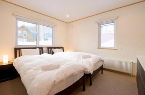 a bedroom with a bed with white sheets and two windows at Ruby Chalet in Niseko