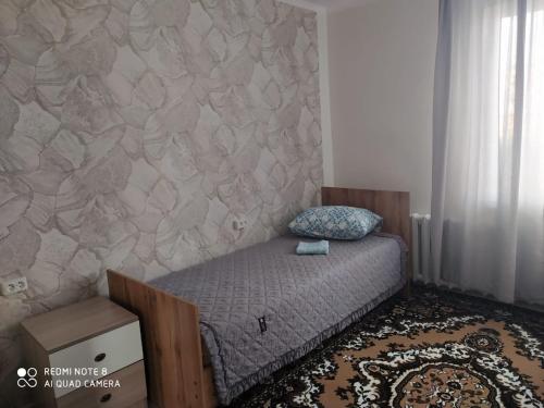 a small bed in a bedroom with a stone wall at SunRay Guest House-Hostel in Karakol