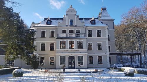 a large white building with snow on the ground at Hotel Fryderyk in Duszniki Zdrój