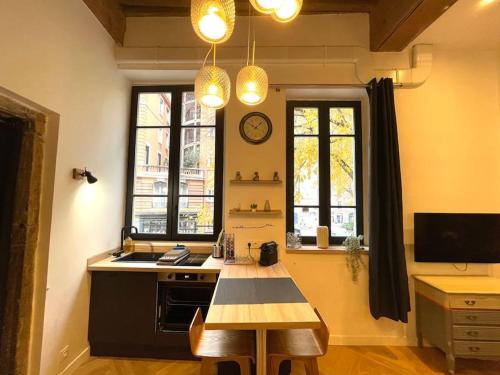 een keuken met een tafel, een wastafel en 2 ramen bij Logement de charme avec balnéo in Lyon