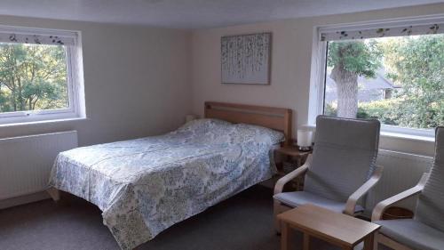 ein Schlafzimmer mit einem Bett und einem Stuhl sowie zwei Fenstern in der Unterkunft Old Orchard Studio in Froggatt