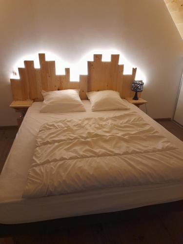 un grand lit blanc avec une grande tête de lit en bois dans l'établissement Gite Le Ranch 6 pers, à Tirepied