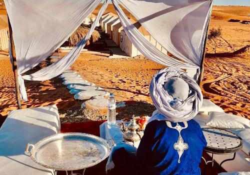 a woman sitting in front of a tent in the desert at Merzouga best camp in Merzouga