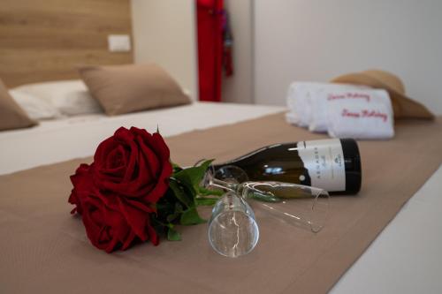 a bottle of wine and a red rose on a bed at MARE e Terra Holiday fronte mare in San Vito lo Capo