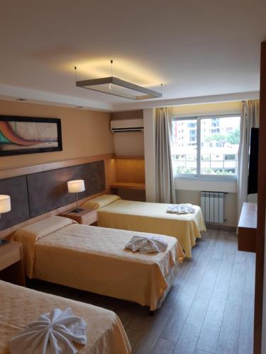 a hotel room with three beds and a window at Hotel Presidente in Villa Carlos Paz