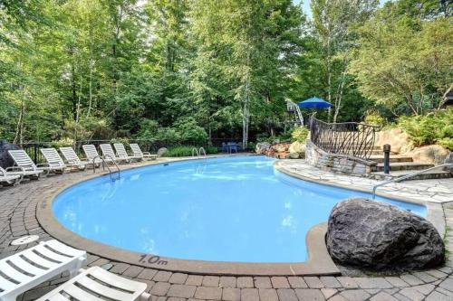a large swimming pool with chairs and a rock at Chalet-Style Condo - 5 minutes to Lifts and village! in Mont-Tremblant