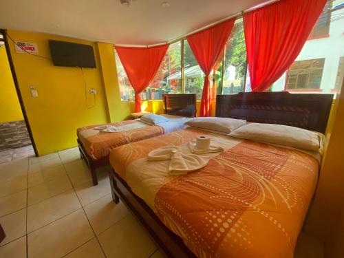 2 camas en una habitación de hotel con cortinas rojas en Hostal Maria Mercedes, en Baños
