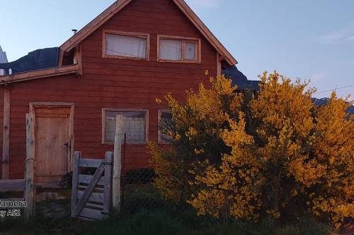 una casa roja con una puerta y un árbol en La Joaquina, Casa de montaña. en El Chaltén