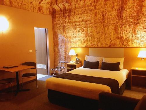 Habitación de hotel con cama grande y escritorio. en Desert Cave Hotel, en Coober Pedy