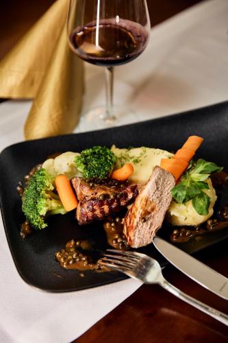 a plate of food with meat and vegetables and a glass of wine at Hotel Maraton in Bydgoszcz