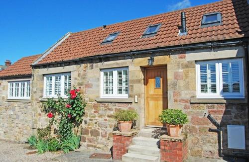 a brick house with a wooden door and flowers at Martins Cottage in Alnmouth