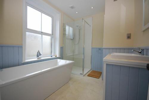 baño con bañera y ducha y ventana en Coastal Haven, en Seahouses