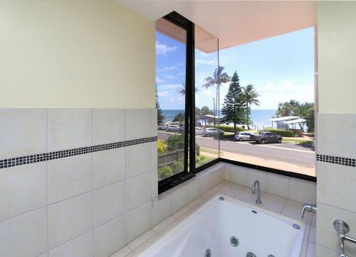 eine Badewanne im Bad mit einem großen Fenster in der Unterkunft Coral Sands Apartment 201 in Bargara