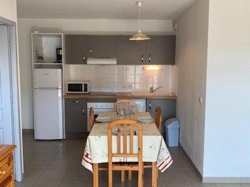 Il comprend une cuisine équipée d'une table avec des chaises et d'un réfrigérateur blanc. dans l'établissement Appartement F3 avec balcon & terrasse, proche plage, 6 couchages - Narbonne Plage - FR-1-229B-23, à Narbonne