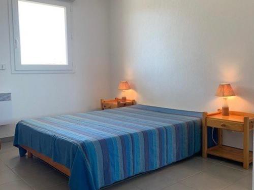 - une chambre avec un lit avec une couverture bleue et 2 tables dans l'établissement Appartement F3 avec balcon & terrasse, proche plage, 6 couchages - Narbonne Plage - FR-1-229B-23, à Narbonne