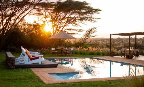 a swimming pool with chairs and a table and the sunset at Ololo Safari Lodge & Farm in Nairobi