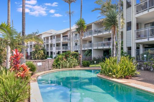 a swimming pool in front of a building with palm trees at Sunrise Cove- 2BR Waterfront Apartment by uHoliday in Kingscliff