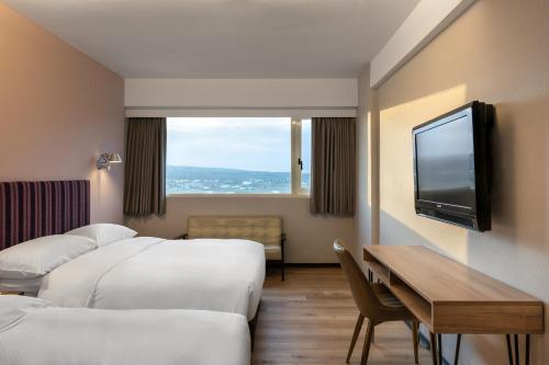 a hotel room with three beds and a table and a tv at River Inn Kenting in Hengchun