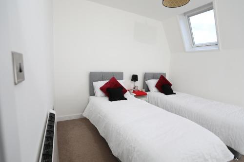 two beds in a white room with red pillows at Plush 2-bedroom apartment Coventry city center in Coventry