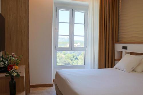 a bedroom with a white bed and a window at Le Royal Hôtel Restaurant in Bonifacio