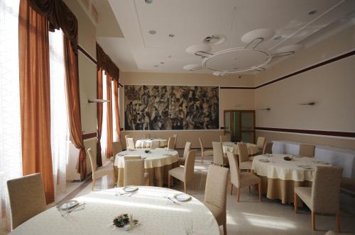 uma sala de jantar com mesas e cadeiras brancas e um mural em Hotel Royal em Senta