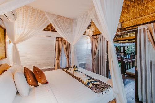 - une chambre avec un lit blanc et des rideaux dans l'établissement Alam Nusa Bungalow Huts & Spa, à Nusa Lembongan