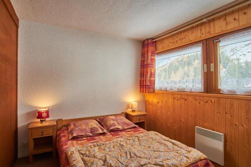 a bedroom with a bed and two night tables and two windows at Appartement au pied des pistes in Saint-Martin-de-Belleville