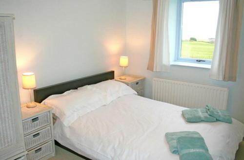 a bedroom with a white bed with two lamps and a window at Longstone in Embleton