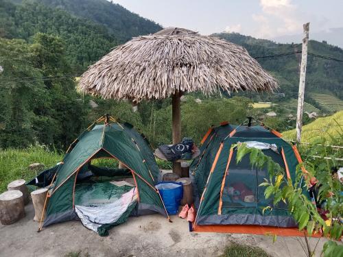 two tents sitting under a straw umbrella at Bình Minh Homestay in Nam Giang