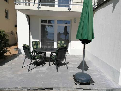 un patio con mesa, sillas y una sombrilla verde en Haus am Kölpinsee App 1 4 en Kölpinsee