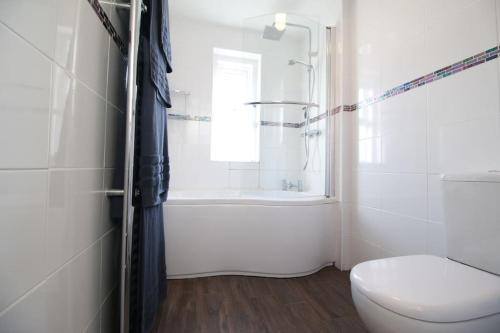 a white bathroom with a toilet and a tub and a window at Beachy Head Apartment By Air Premier in Seaford