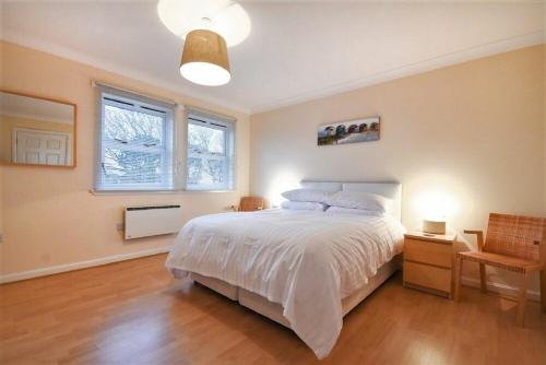 a bedroom with a white bed and two windows at Beachcomber Apartment in Bamburgh