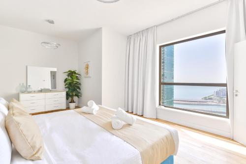 a white bedroom with a large window and a bed at Luxury JBR · Full Sea View · Free 5* Beach Resorts Access in Dubai