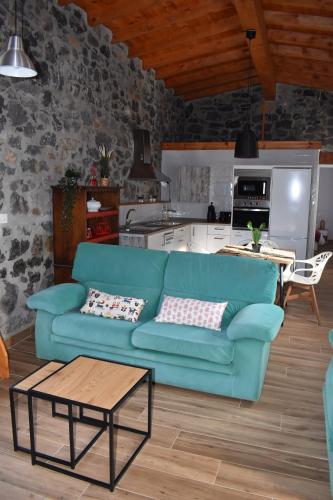 a living room with a blue couch and a kitchen at La Antigua Cuadra es un alojamiento de piedra y altos techos de madera con mucho encanto, jardín privado con barbacoa y acceso al río Asón in Ramales de la Victoria
