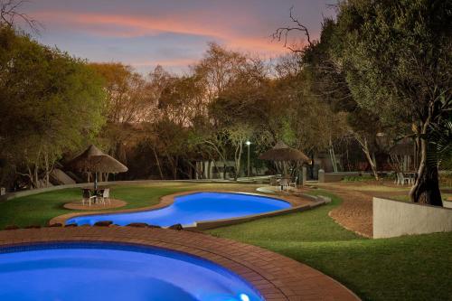 une grande piscine bleue dans une cour arborée dans l'établissement Premier Hotel Roodevalley, à Pretoria