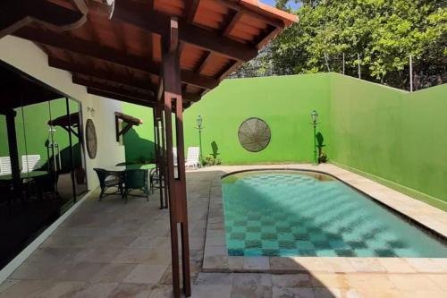 a swimming pool with a green wall and a wooden roof at VILLA RANIERI in Pipa