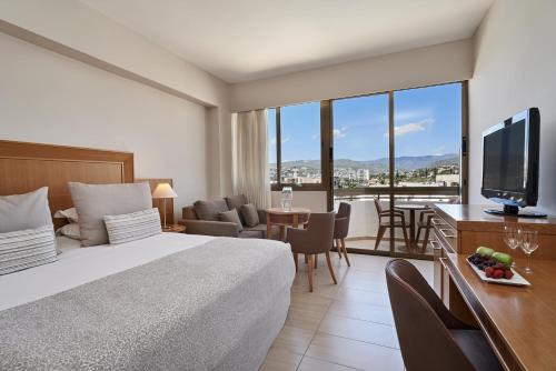 Cette chambre comprend un lit et un bureau avec une télévision. dans l'établissement Atlantica Oasis Hotel, à Limassol
