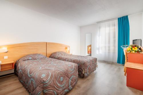 a hotel room with two beds and a desk at Hôtel Ariane in Lourdes