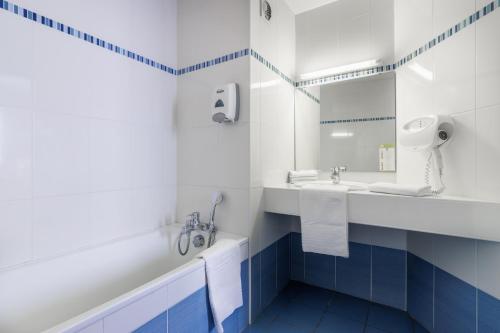 a bathroom with a tub and a sink and a mirror at Hôtel Ariane in Lourdes