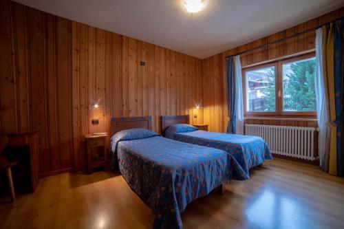 two beds in a room with wooden walls and a window at Family Apartments Le Chalet in Champoluc