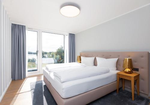 a white bedroom with a large bed and a window at Maremüritz Yachthafen Resort in Waren