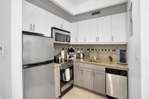 una cocina con armarios blancos y electrodomésticos de acero inoxidable en National at 888 Sixth Avenue - Furnished Apartments, en Nueva York