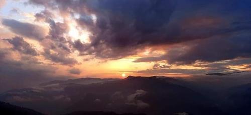 a cloudy sky with the sun setting behind a mountain at Swastika Homestay and Travels Kurseong Bazar Near HDFC Bank NH55 Road Kurseong in Kurseong