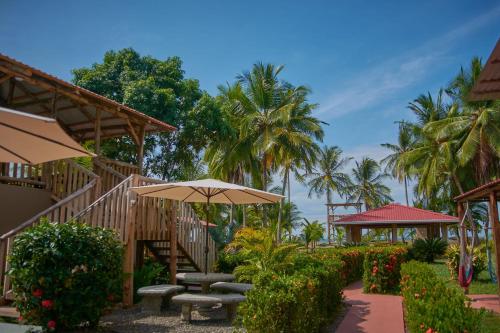 a patio with benches and an umbrella and palm trees at Tranquilidad Resort in Parrita