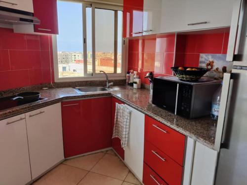 a red kitchen with a sink and a microwave at Appartement très proche Rabat et de l'Aéroport in Salé