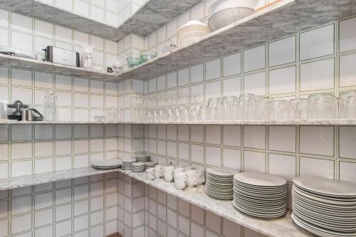 una cucina bianca piastrellata con piatti e bicchieri su scaffali di ES GANXO HOUSE PORTO CRISTO a Porto Cristo