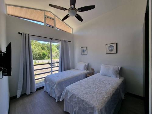 two beds in a room with a window and a ceiling fan at Casa Cardumen - Ciudad Del Mar, in Jaco in Jacó